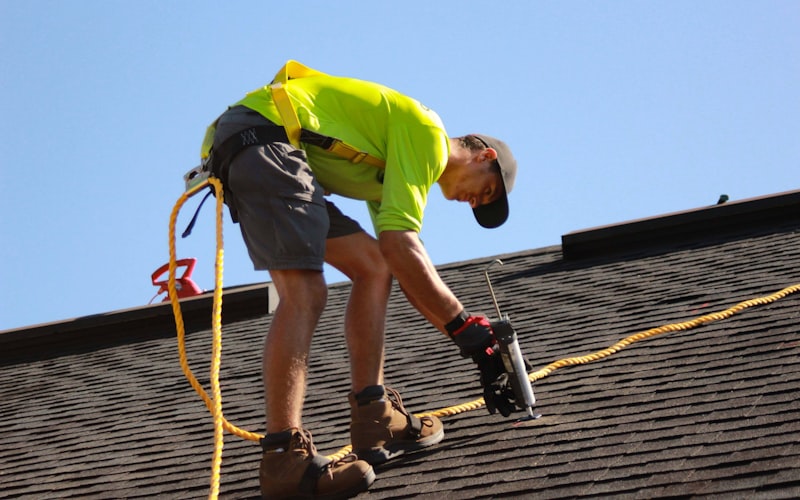 Professional roofer using power drill on roof shingles